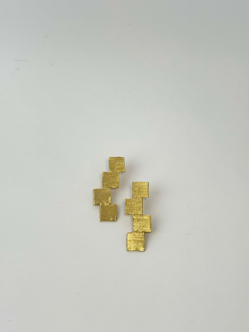 Gold square earrings on a light gray background