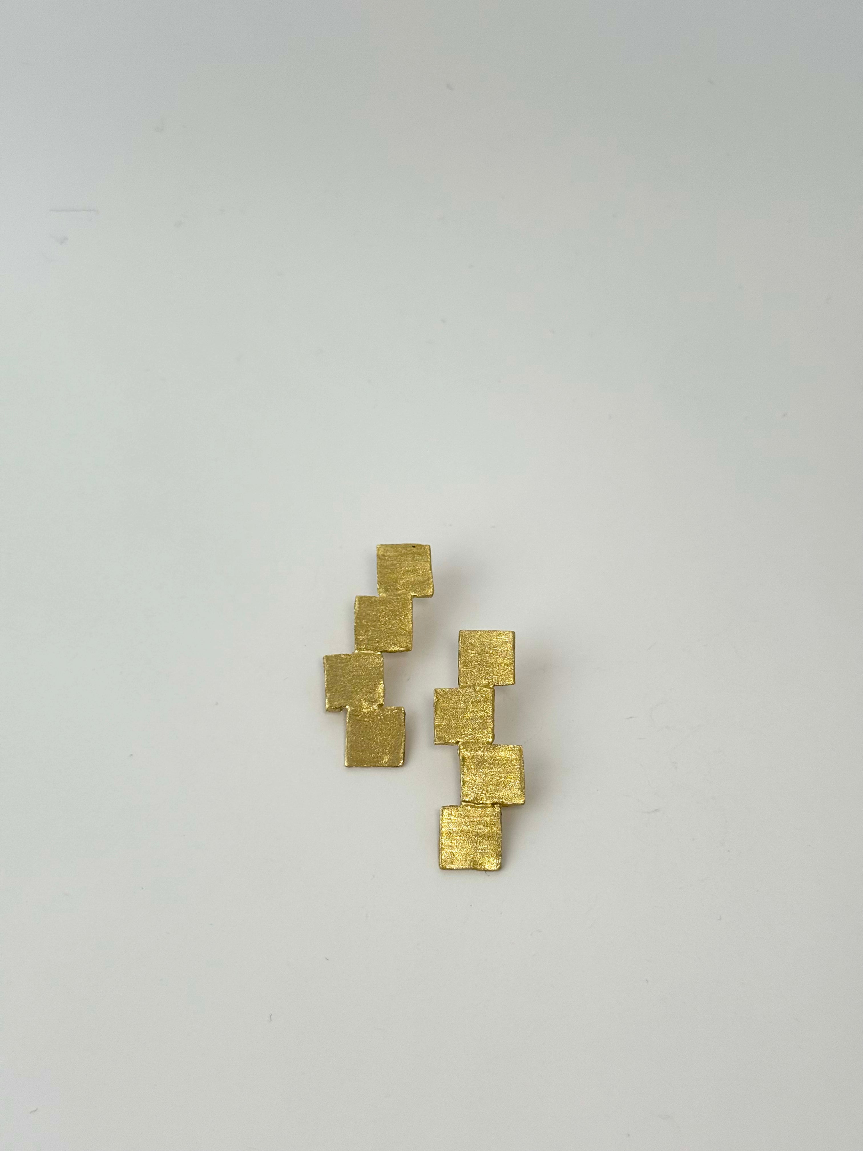 Gold square earrings on a light gray background